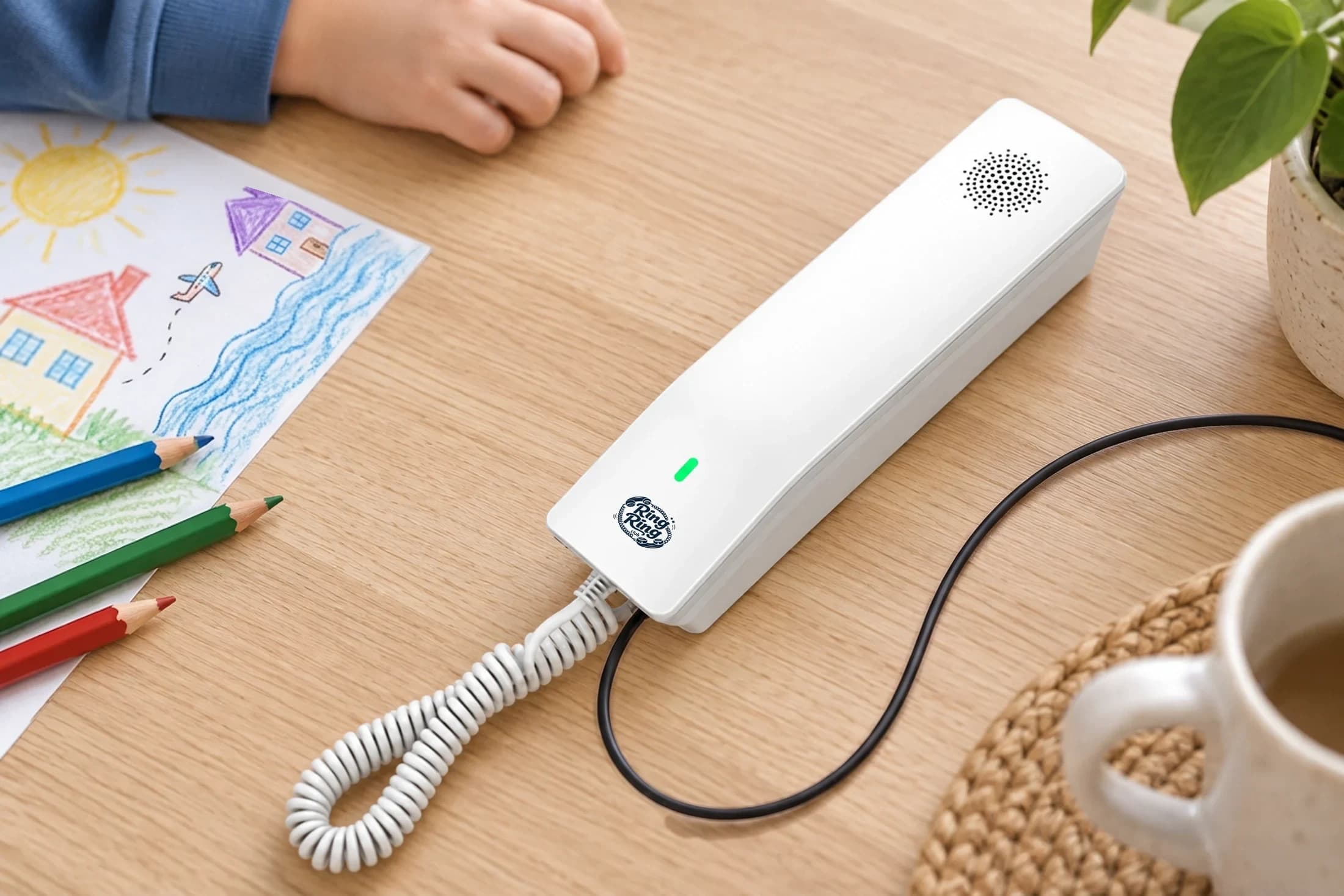 White Ring Ring Modern phone on a family table beside a child’s drawing of two houses across the sea, with a little plane between them